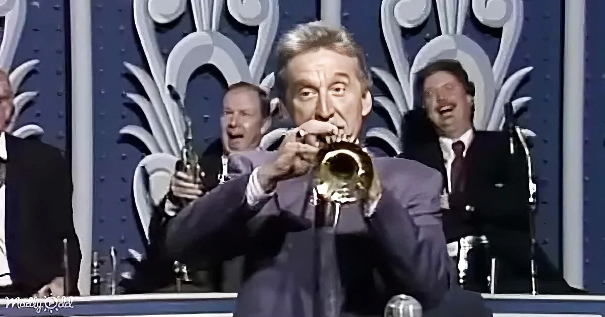 A man in a suit plays a trumpet on stage, surrounded by other musicians.