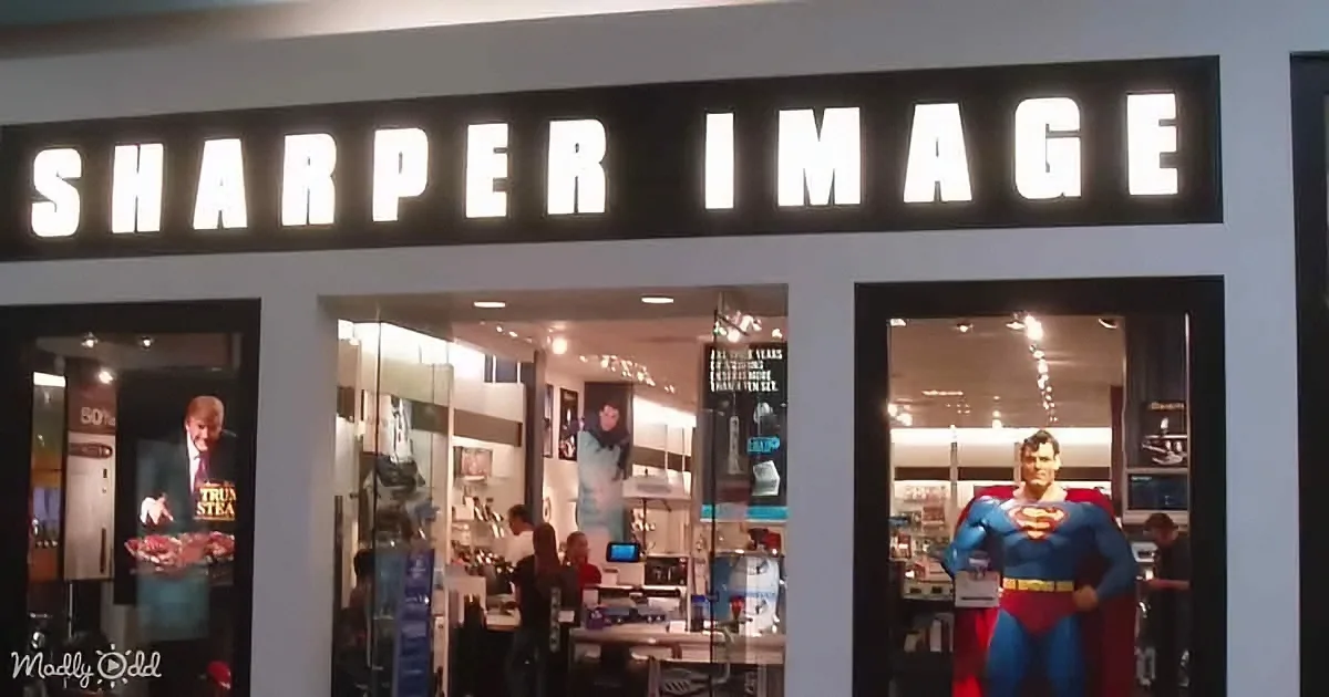 A Sharper Image store displays a Superman statue in its window, with people inside browsing.