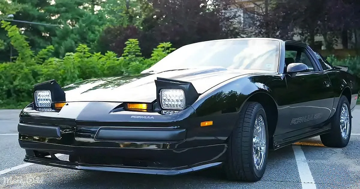 A sleek black Pontiac Firebird with a glossy finish and chrome wheels is parked in a lot.