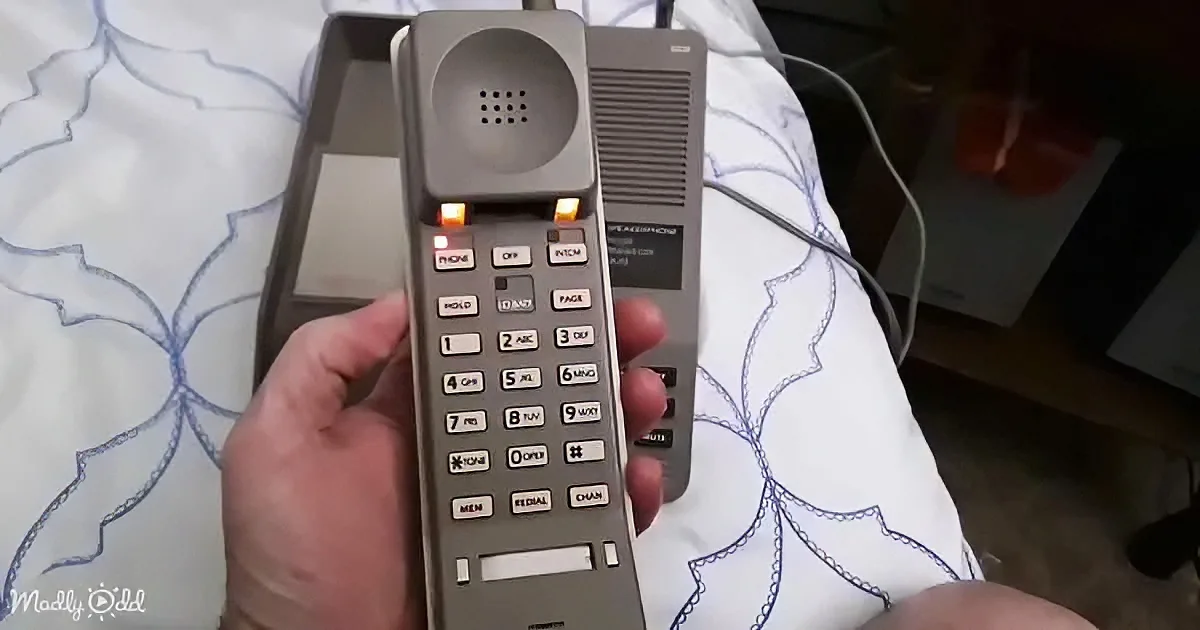 A hand holds a vintage corded telephone with illuminated buttons and a speakerphone, resting on a patterned surface.