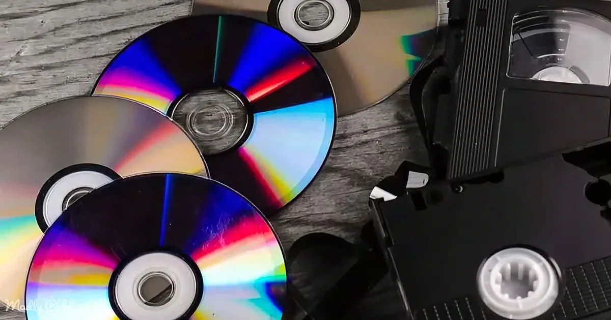 A pile of colorful CDs and a black VHS tape on a wooden surface.