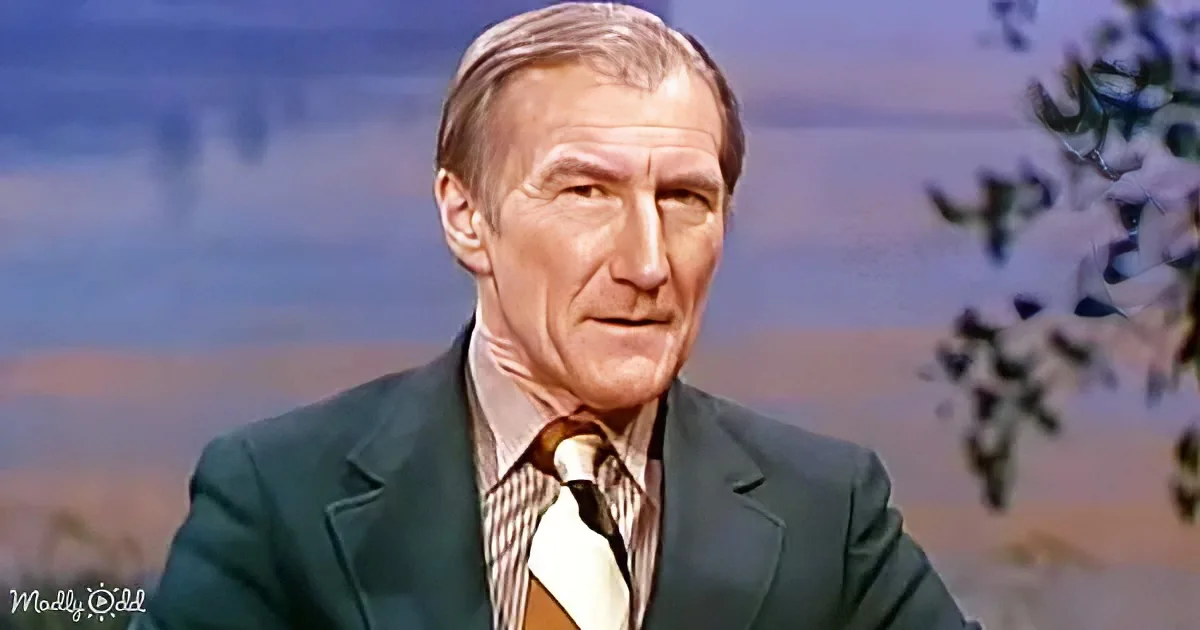 A man in a green suit and striped tie sits against a scenic backdrop, looking directly at the camera.