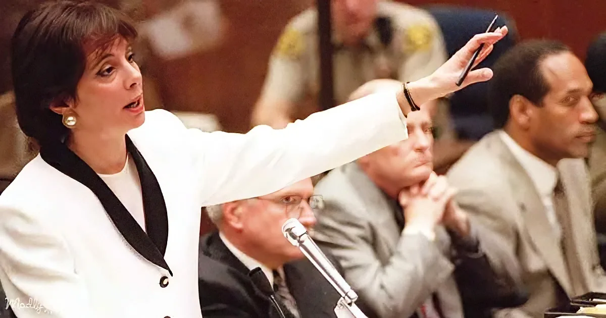 A woman in a white suit gestures emphatically while speaking at a formal meeting.