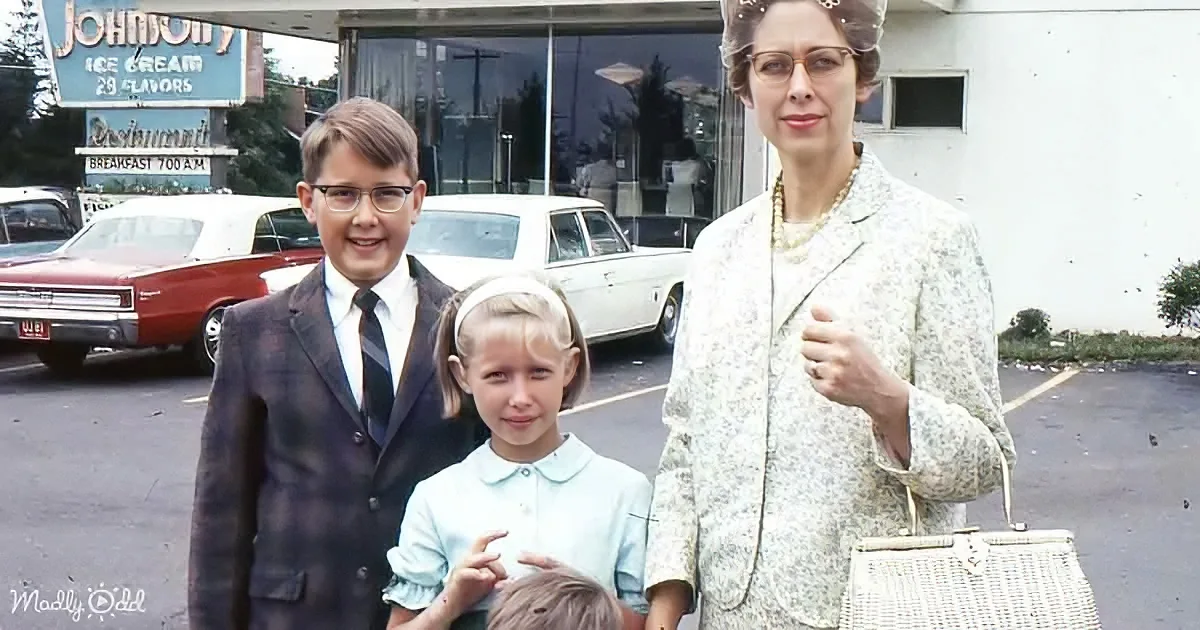 A woman in a floral suit holds a purse, standing with two children in a vintage parking lot.