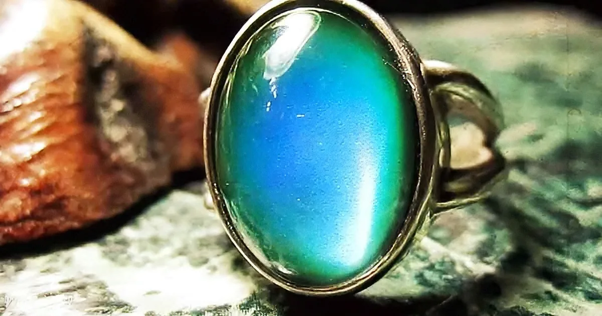 A silver ring with a large, oval, blue-green gemstone sits on a textured surface.