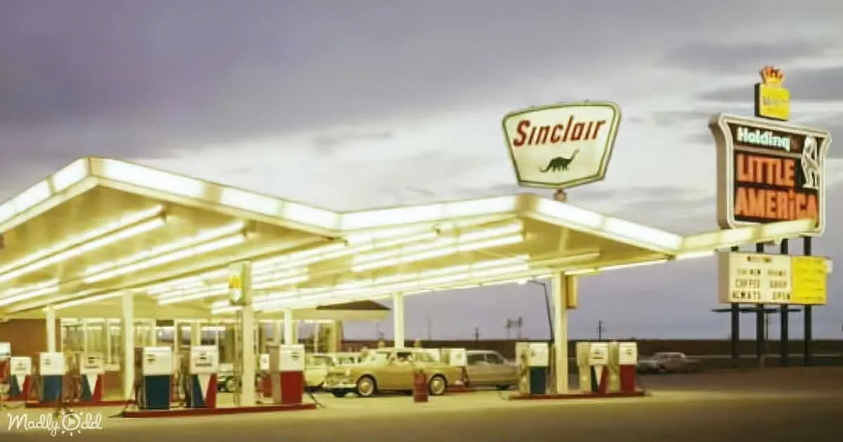 A vintage Sinclair gas station with illuminated pumps and classic cars at dusk.