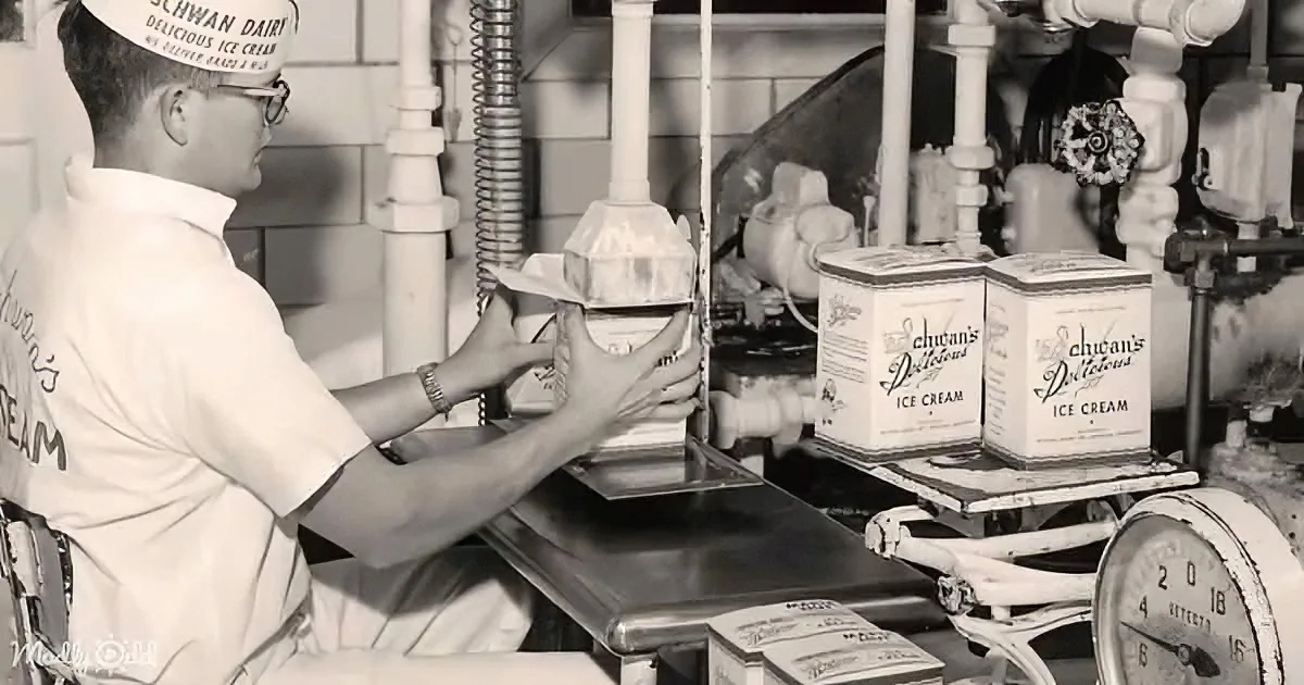 A man in a Schwan Dairy uniform fills ice cream into a cone at a counter.