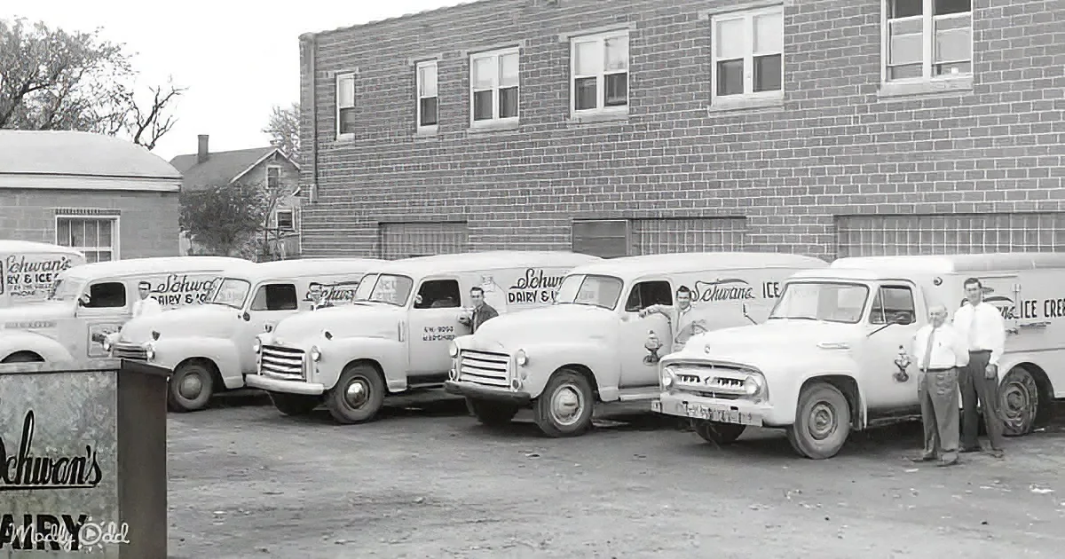 Schwan's delivery trucks lined up in front of a brick building with two men standing nearby.