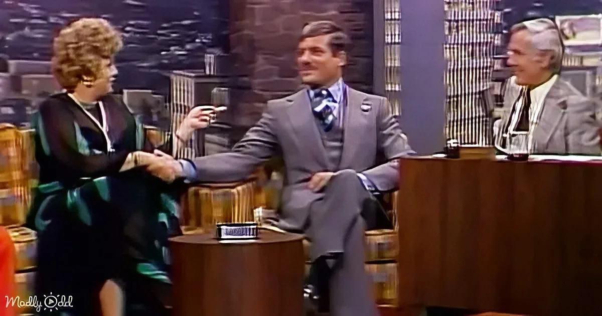 A woman in a green dress shakes hands with a man in a suit on a talk show set.