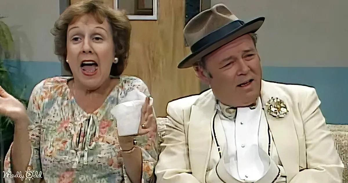 A woman in a floral dress holds a cup, while a man in a white suit and fedora sits beside her, both appearing surprised.