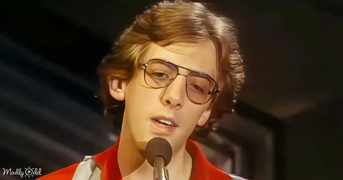 A person wearing a red shirt and glasses is singing into a microphone.