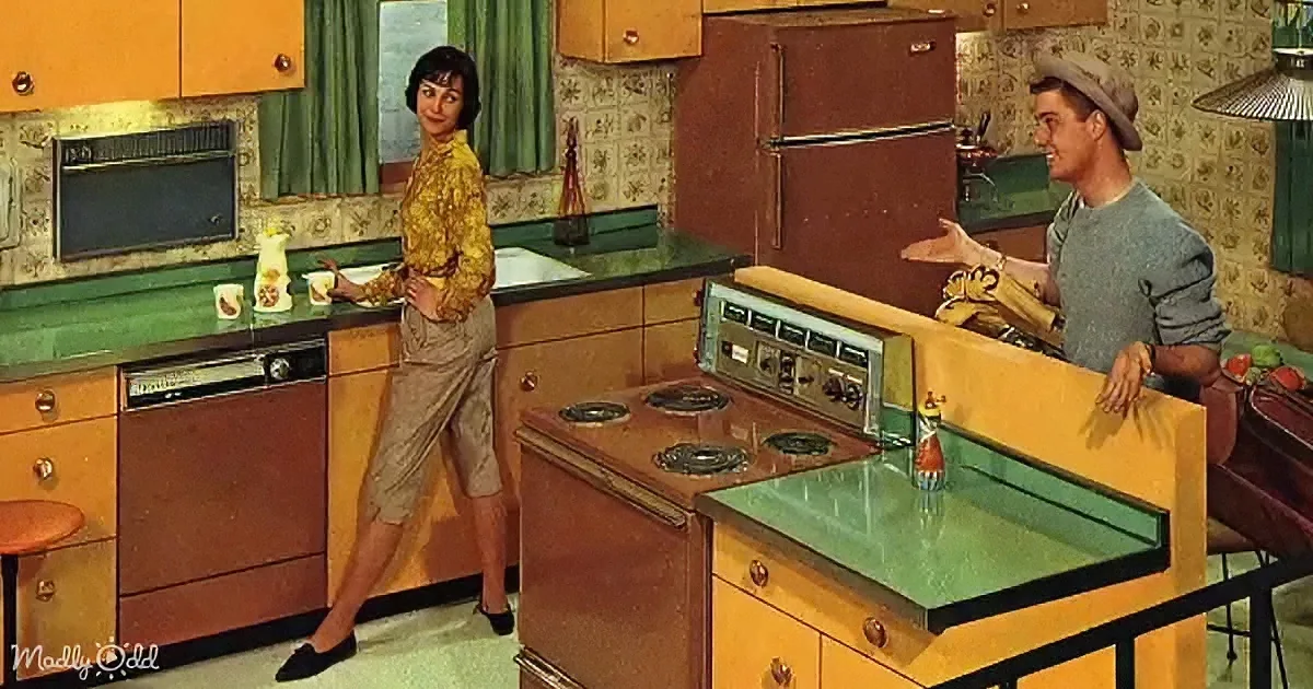 A man and woman in a retro kitchen with green countertops, orange cabinets, and vintage appliances.