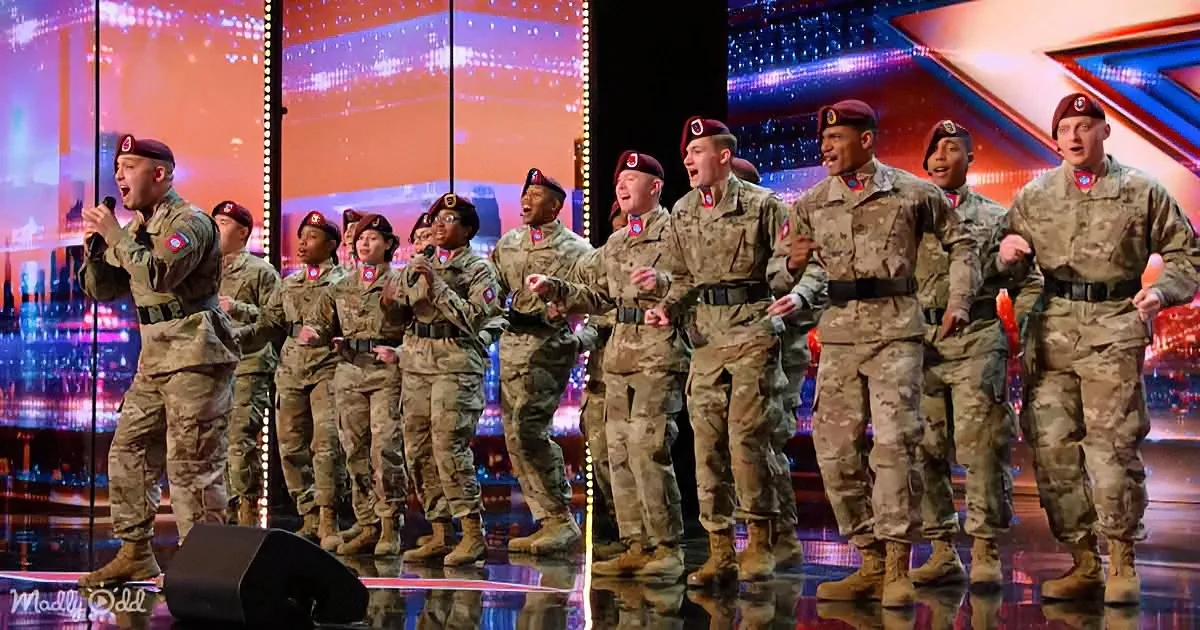 A group of soldiers in camouflage uniforms sing on a brightly lit stage.