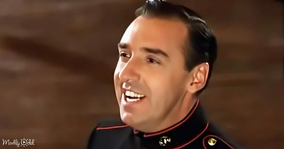 A man in a military uniform with a red collar is smiling, looking to the side.