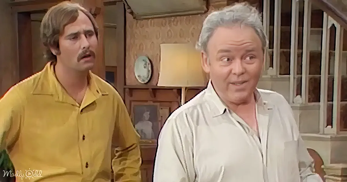 Two men in a room, one in yellow shirt looking concerned, another in white shirt holding papers, both appear to be in a...