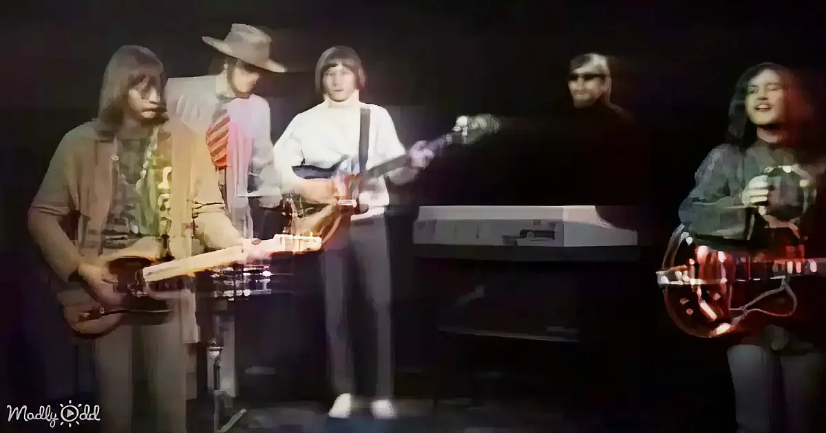 A band performs on stage with guitars, keyboards, and a drum set, under dim lighting.