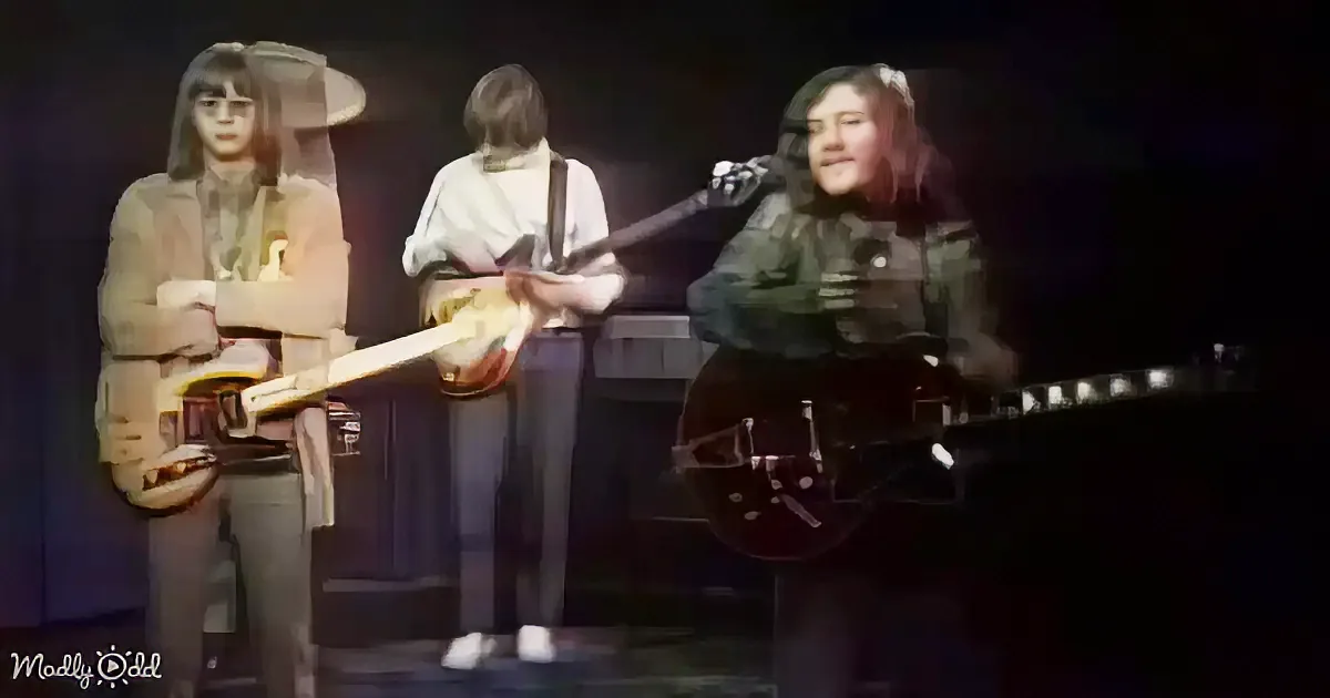 Three individuals on stage, one playing a guitar, another with a microphone, and the third holding a book.