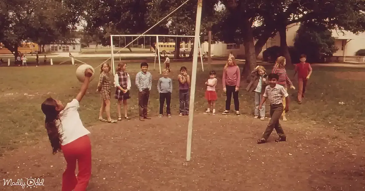 A child in red pants throws a ball while a group of children watches in a park.