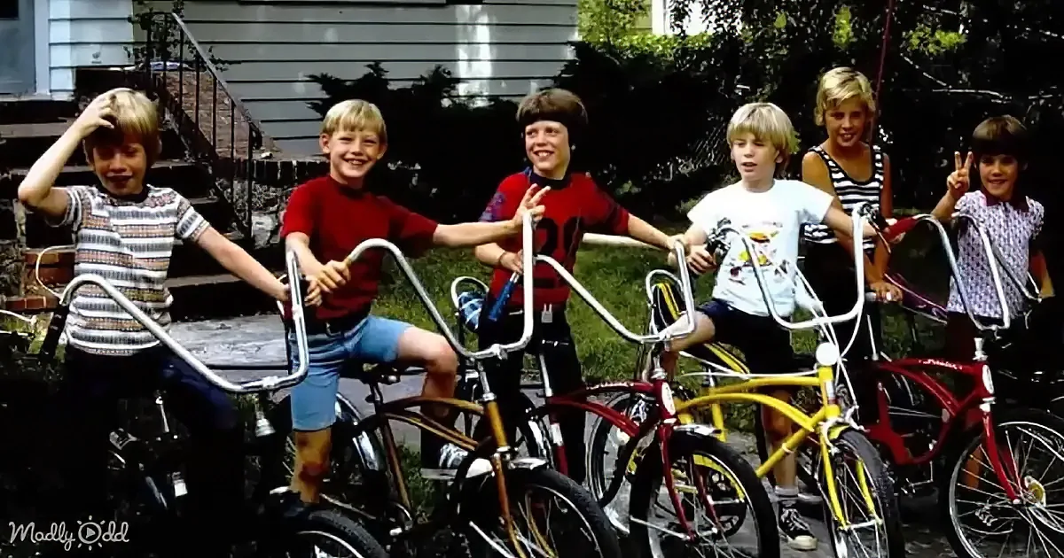 Six children with bicycles smile and pose in front of a house.