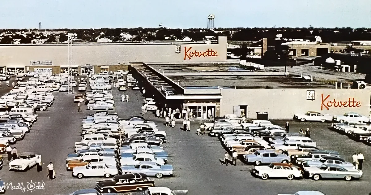 A Korvette store with a large parking lot full of vintage cars and people.