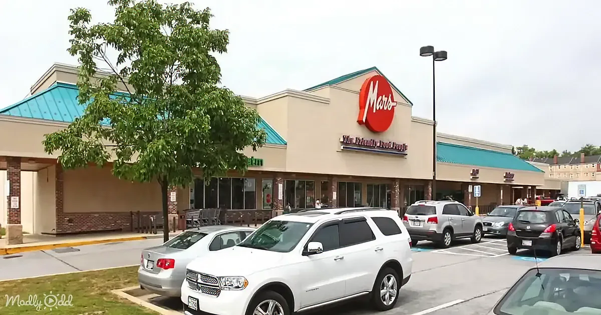 A Mars supermarket with a red logo and blue roof, surrounded by parked cars and a tree.