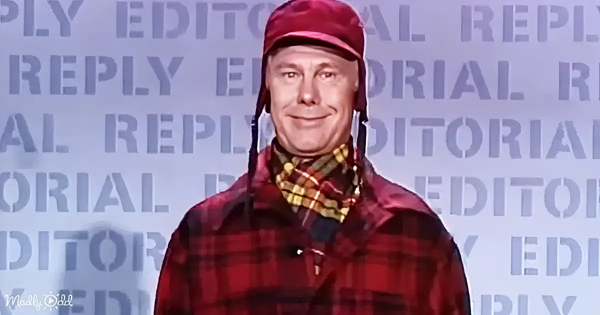 A man in a red plaid shirt and hat stands in front of a backdrop with repeated "EDITORIAL REPLY" text.