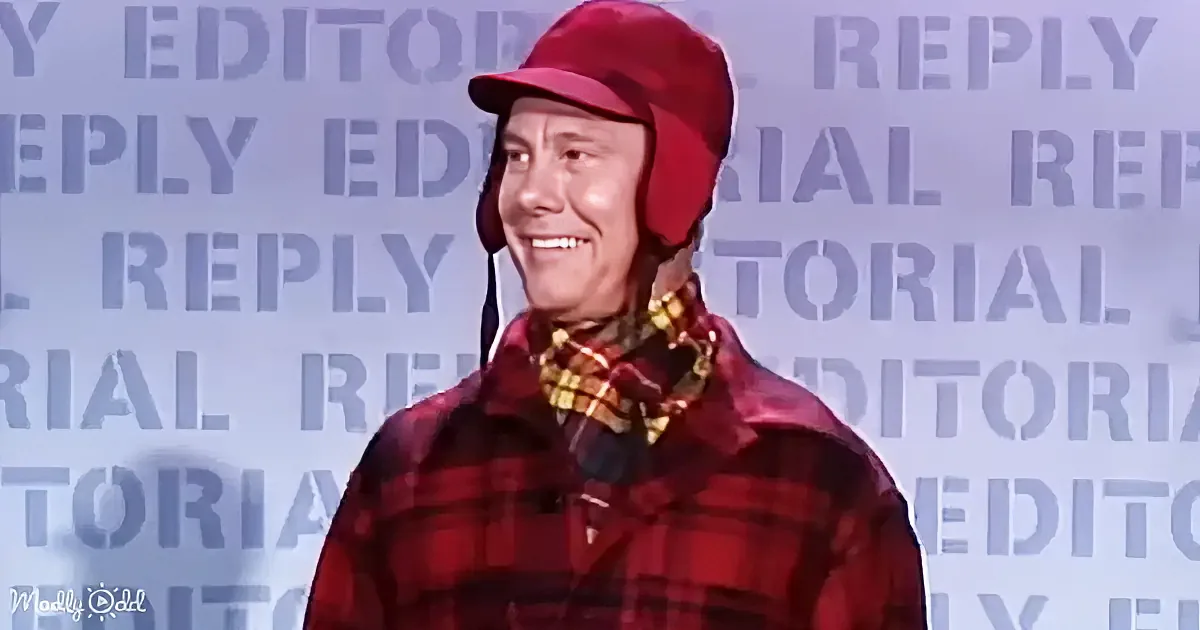 A man in a red plaid shirt and red hat smiles, standing in front of a backdrop with repeated "EDITORIAL REPLY" text.