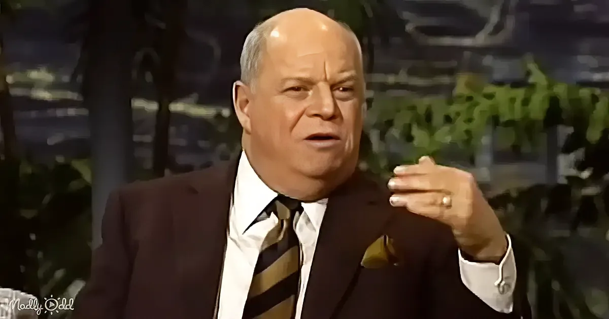 A man in a suit and striped tie gestures with his hand while speaking.