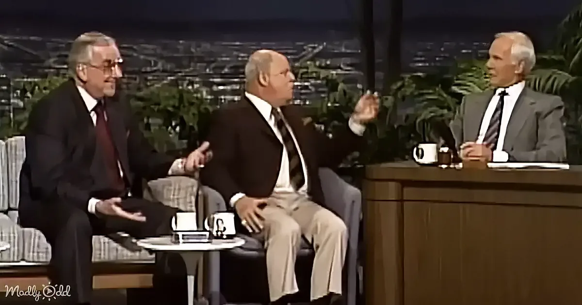 Three men in suits are seated on a talk show set, engaging in conversation.