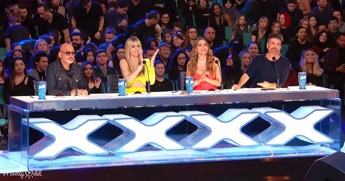 Judges on a panel with a glowing "XXX" sign, audience in the background, colorful setting.