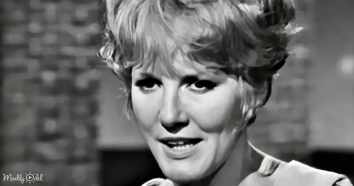 A woman with short, curly hair and a white shirt is smiling in a black-and-white image.