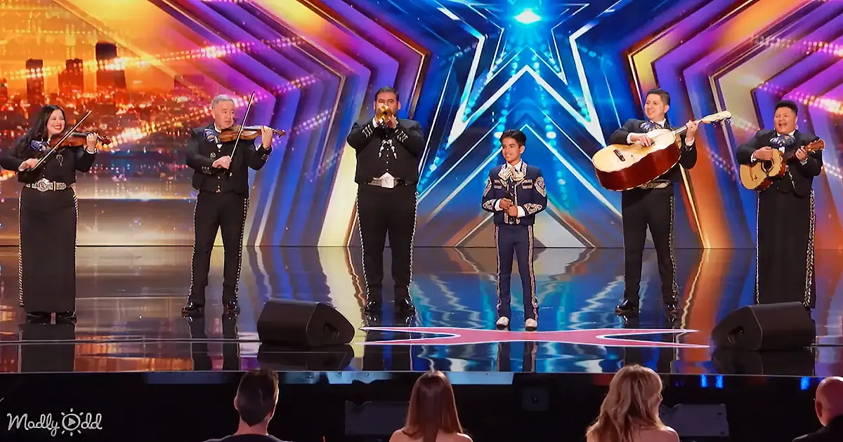 A mariachi band performs on a brightly lit stage with a cityscape backdrop.