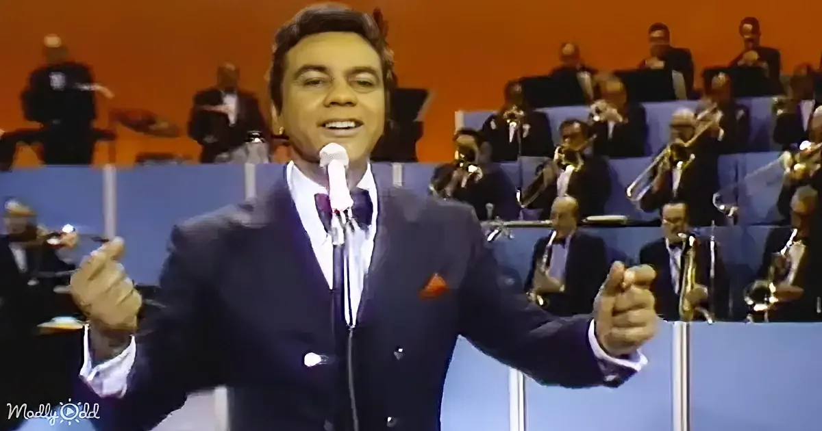 A man in a suit sings into a microphone with a band playing in the background.
