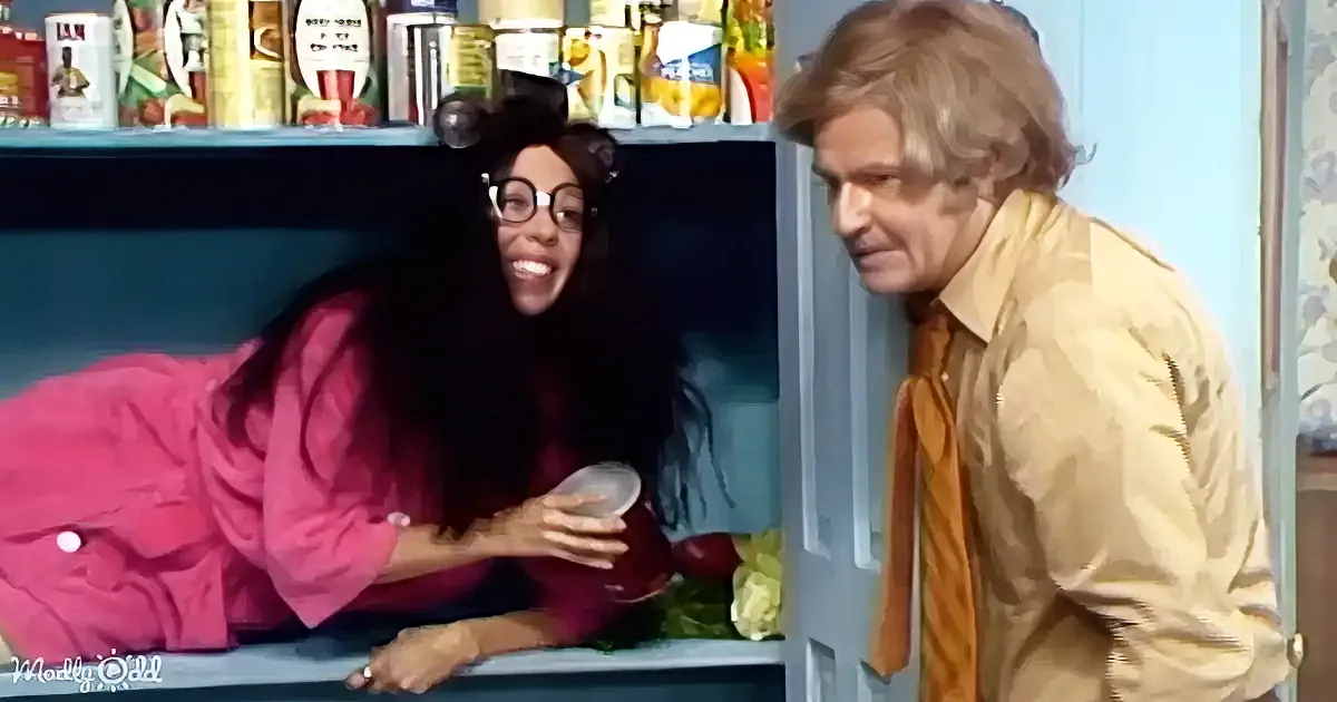 A woman in a pink coat leans on a shelf, smiling, while a man in a yellow shirt looks on.