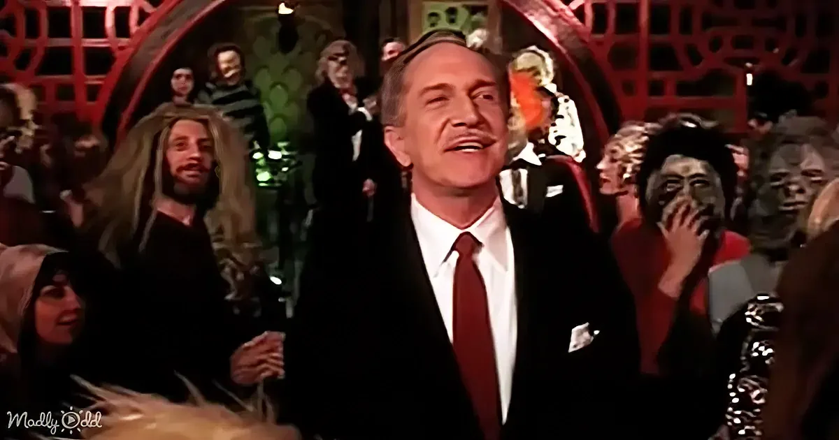 A man in a suit and tie smiles widely, surrounded by a crowd of people in various costumes and expressions.