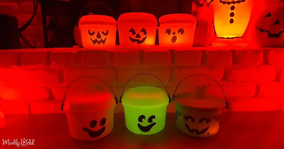 Halloween buckets with glowing faces and pumpkins on a brick wall.