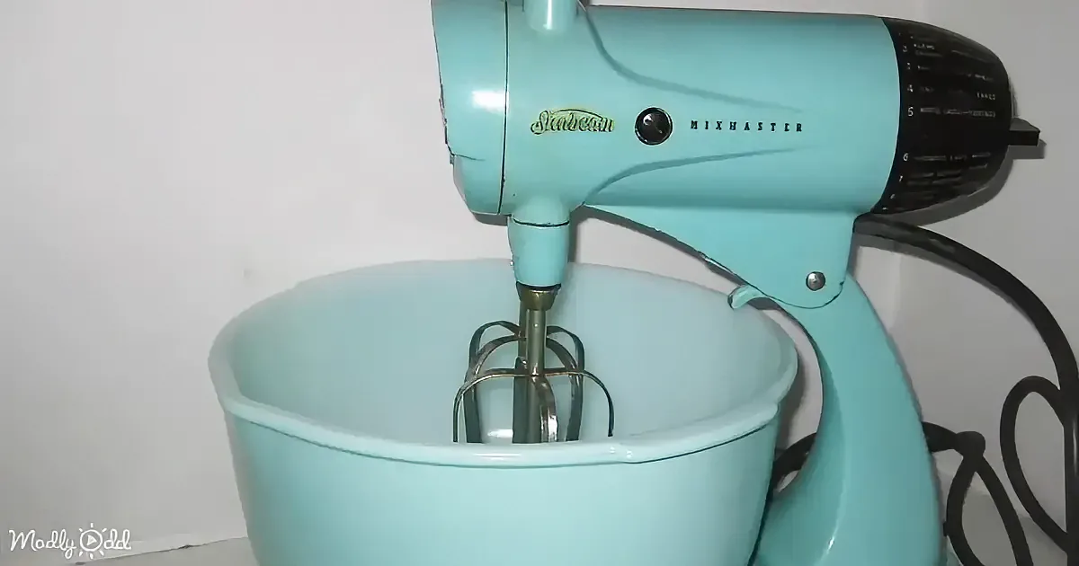 A teal vintage Sunbeam Mixmaster stand mixer with a whisk attachment is shown.