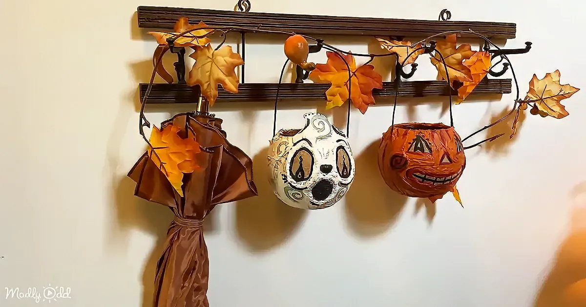 Hanging autumn decorations with leafy garland, pumpkin, skull, and brown fabric basket on a wooden rack.