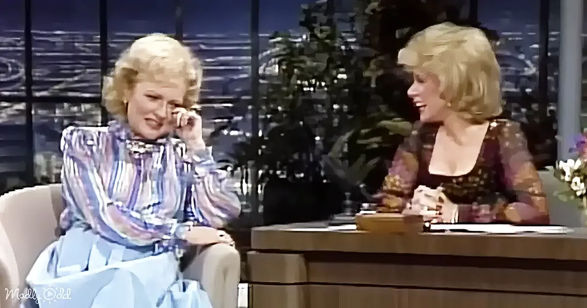 Betty White sits on a talk show set, appearing emotional, while the host smiles beside her.