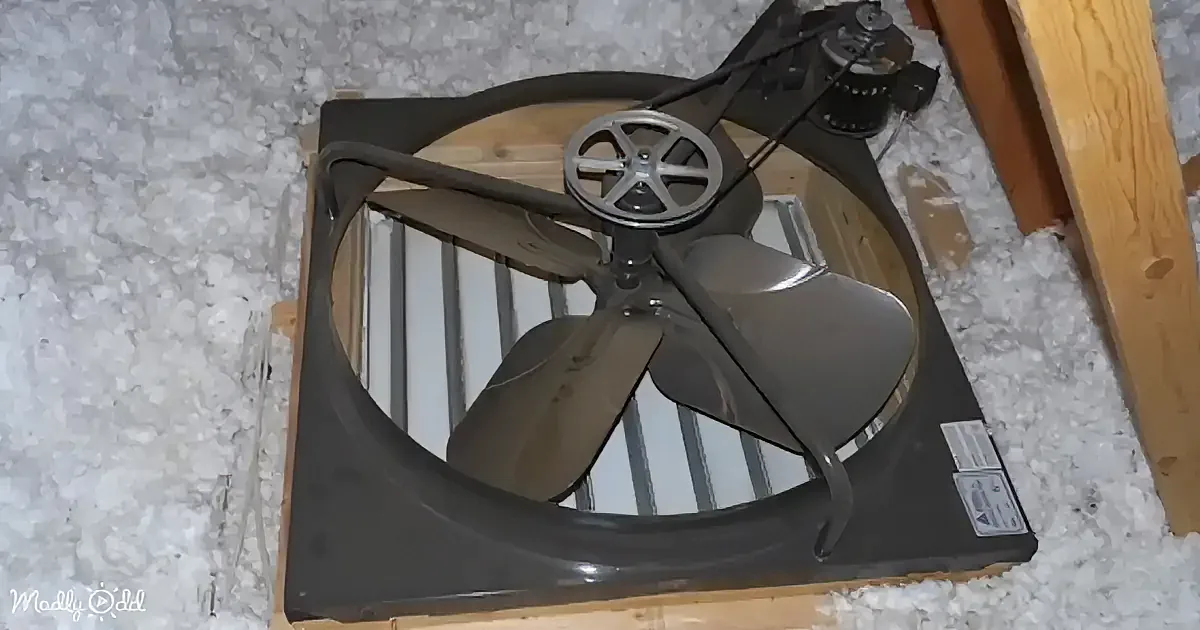 A large industrial fan with a metal frame and blades is mounted on a wooden structure, surrounded by insulation.