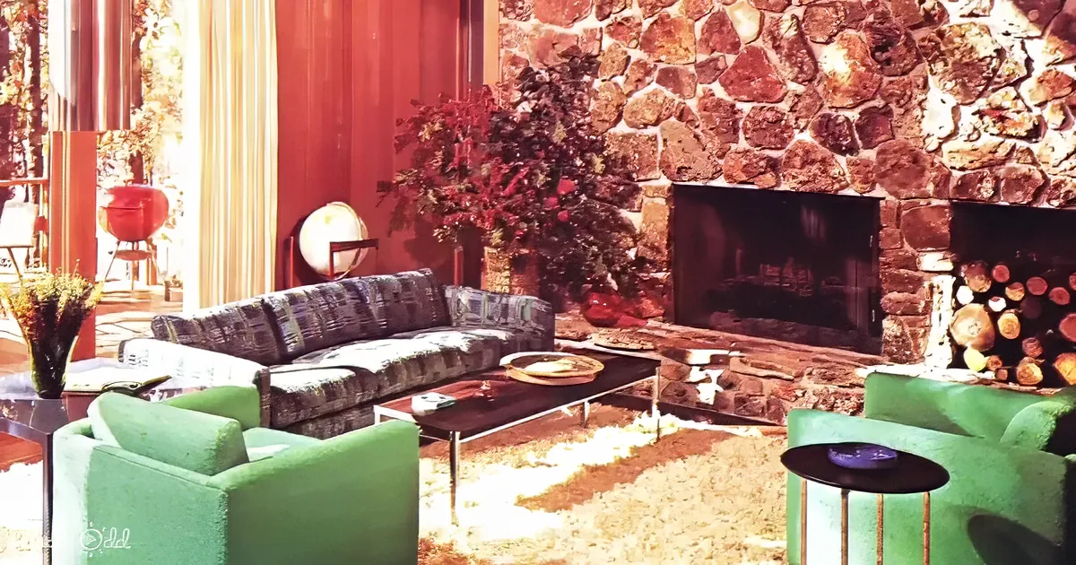 A cozy living room features a stone fireplace, green chairs, a patterned couch, and a festive Christmas tree.