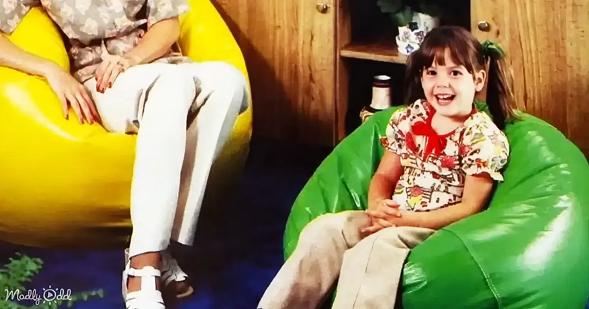 A young girl sits on a green bean bag chair, smiling, while another person sits on a yellow bean bag chair nearby.