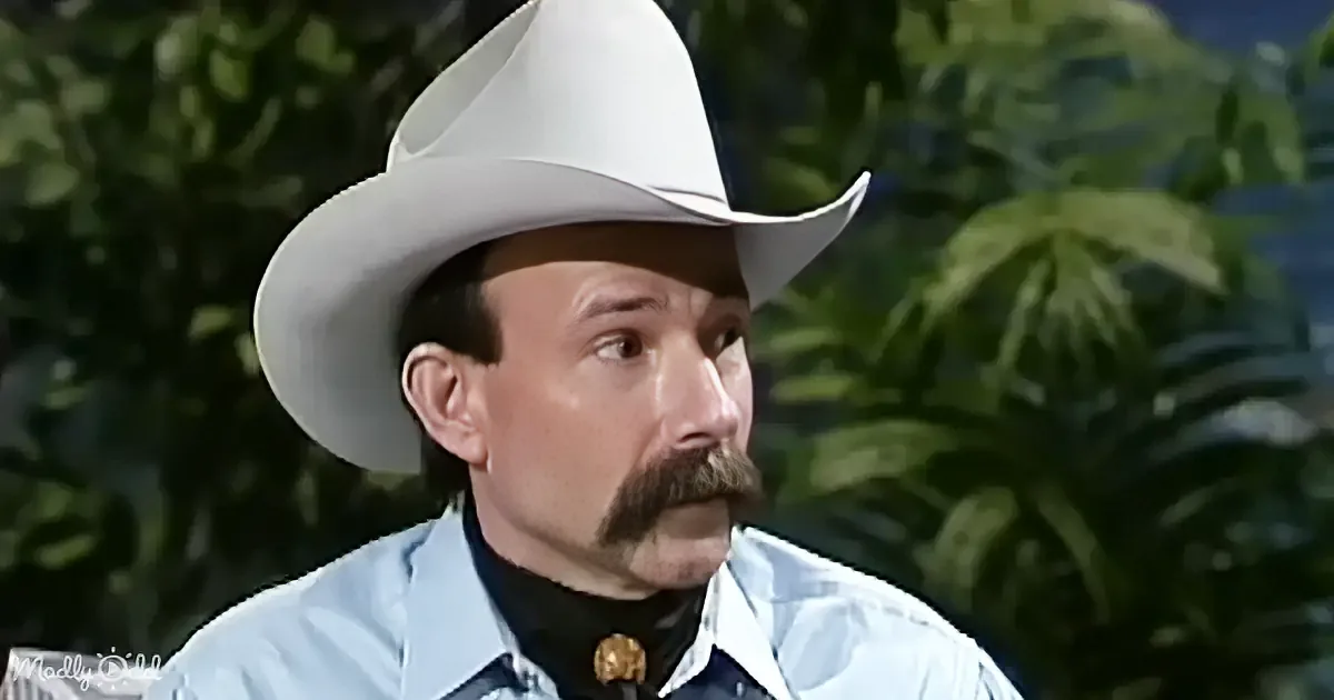 A man wearing a white cowboy hat and a light blue shirt with a black turtleneck underneath is seen against a backdrop of...