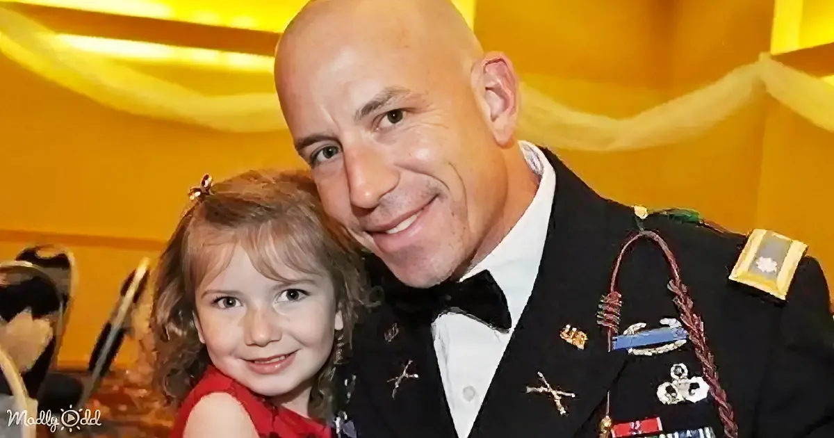 A man in military attire smiles with a young girl in a red dress, both looking at the camera.