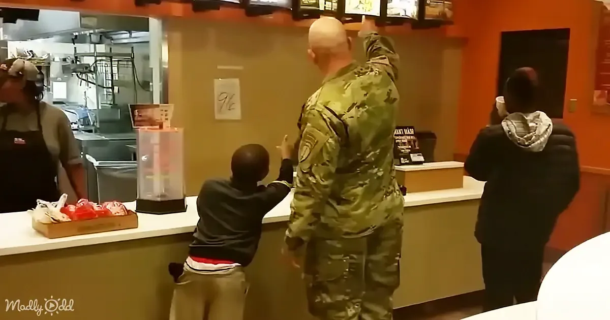 A soldier in camouflage points at a menu while a child stands beside him at a fast-food counter.