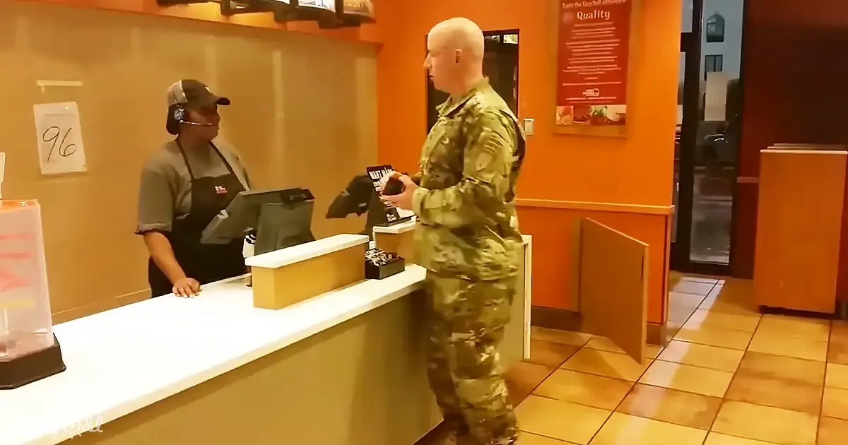 A soldier in camouflage uniform stands at a fast-food counter, interacting with a worker.