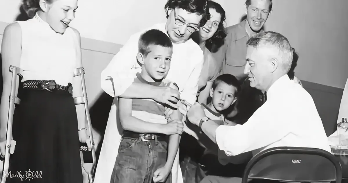 A young boy receives a shot from a doctor, surrounded by family and onlookers.