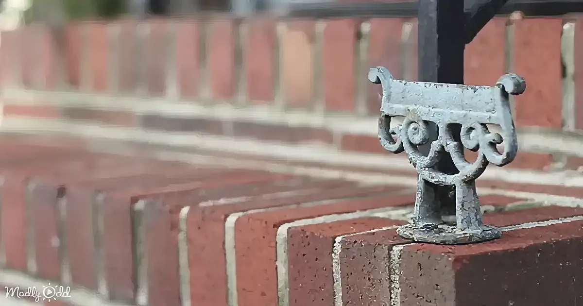 A decorative metal bracket sits atop a red brick wall, with a blurred brick background.