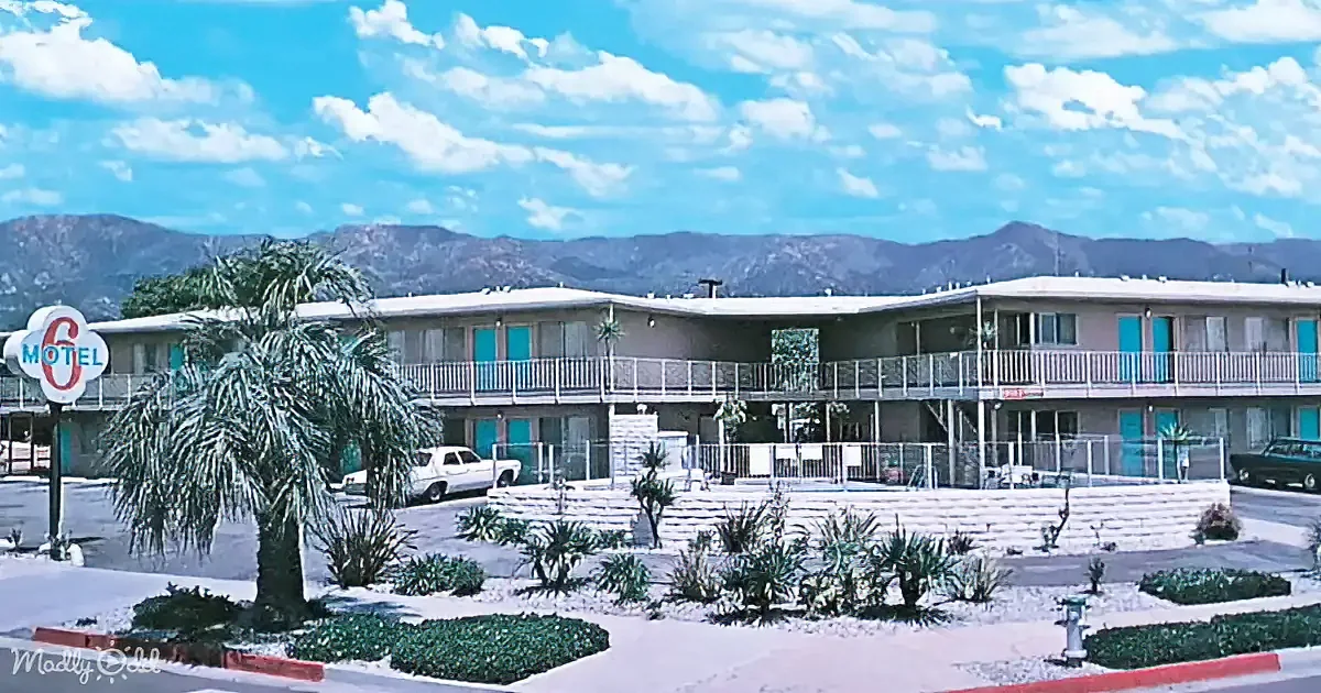A Motel 6 with a palm tree, cars, and mountains in the background under a blue sky.