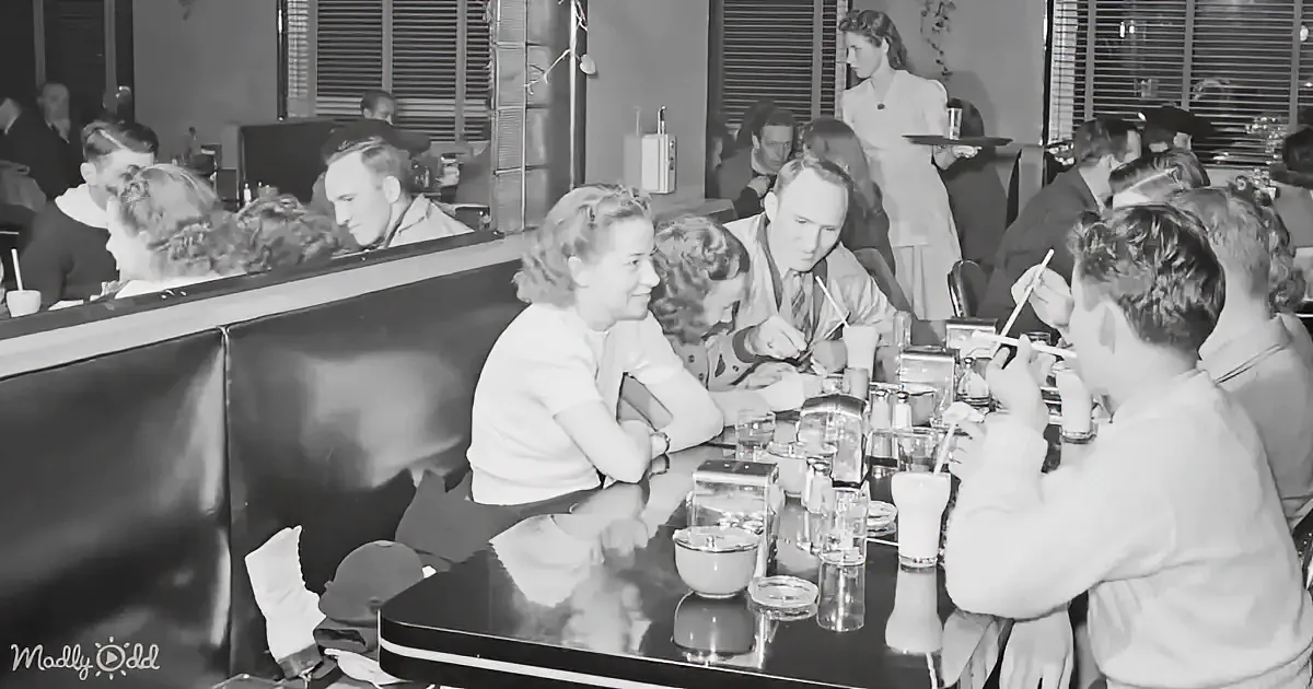A woman in a diner smiles as she sits at a table with drinks and food.